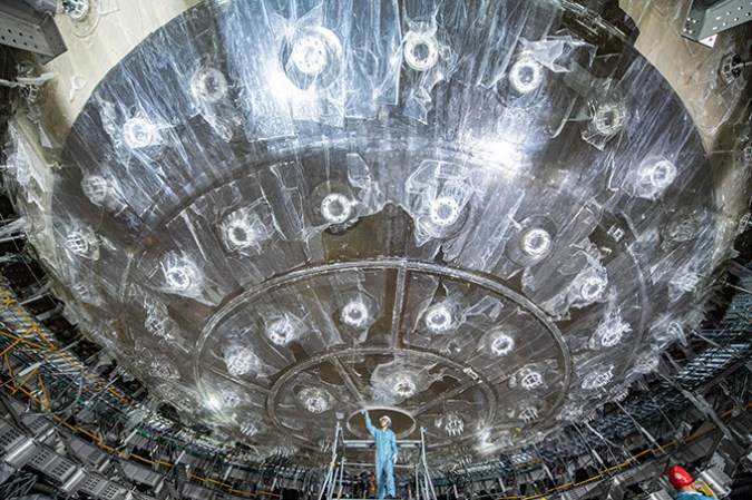 121624_ec_neutrino-detector_slide5 A person stands below an enormous translucent sphere.